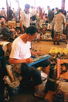 A man in market playing a very strange musical instrument to an image of Mao Zedong